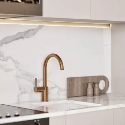 Close-up of a white marble kitchen sink with a brushed gold faucet against a marble backsplash at Atzaro Residences, Playa del Carmen