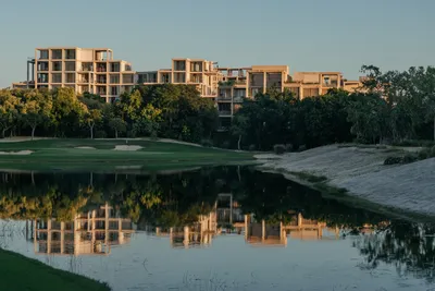 Reflejo de laguna con edificios en The Village Resort & Residences en Corasol, Playa del Carmen